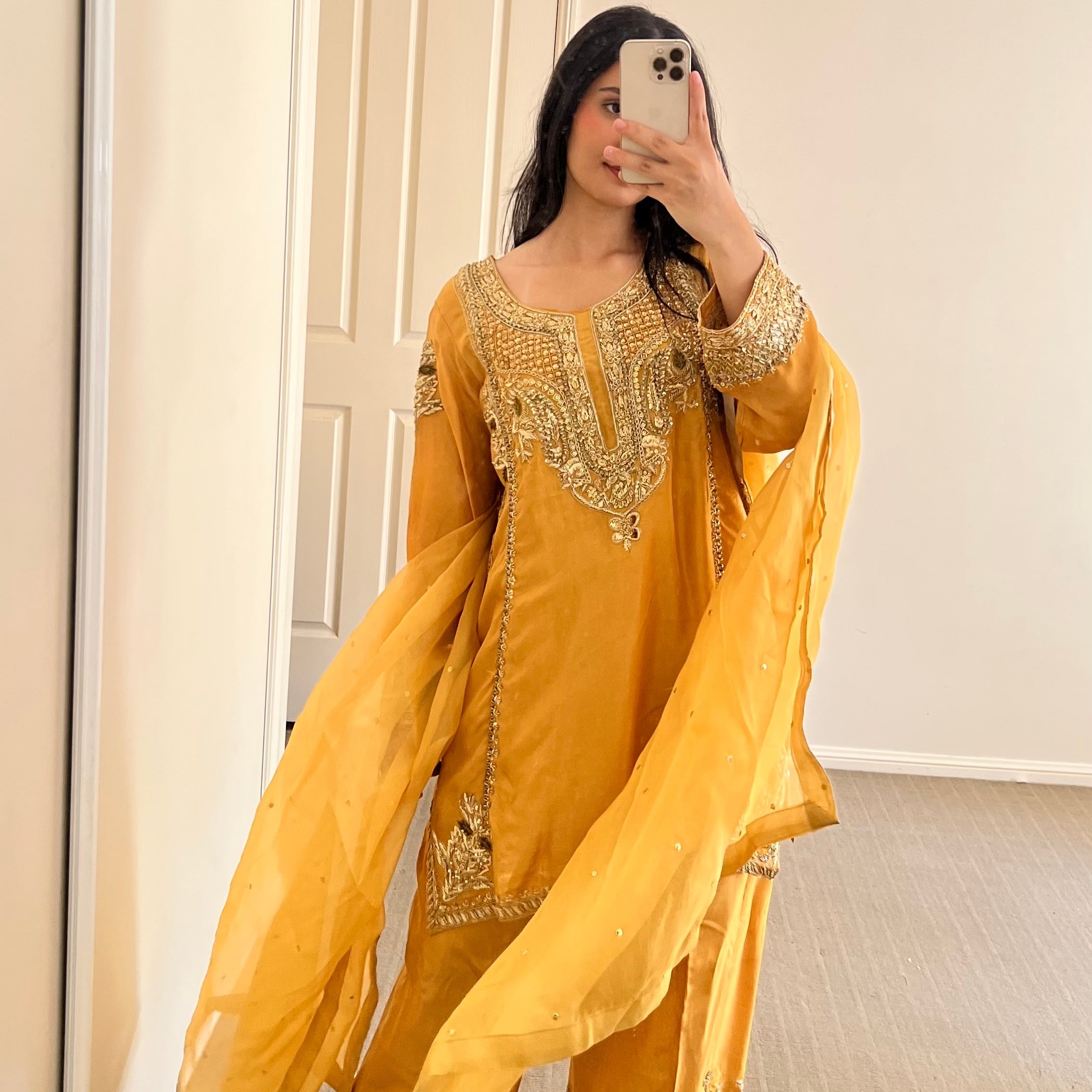 Person wearing a yellow traditional outfit with intricate designs in a room.